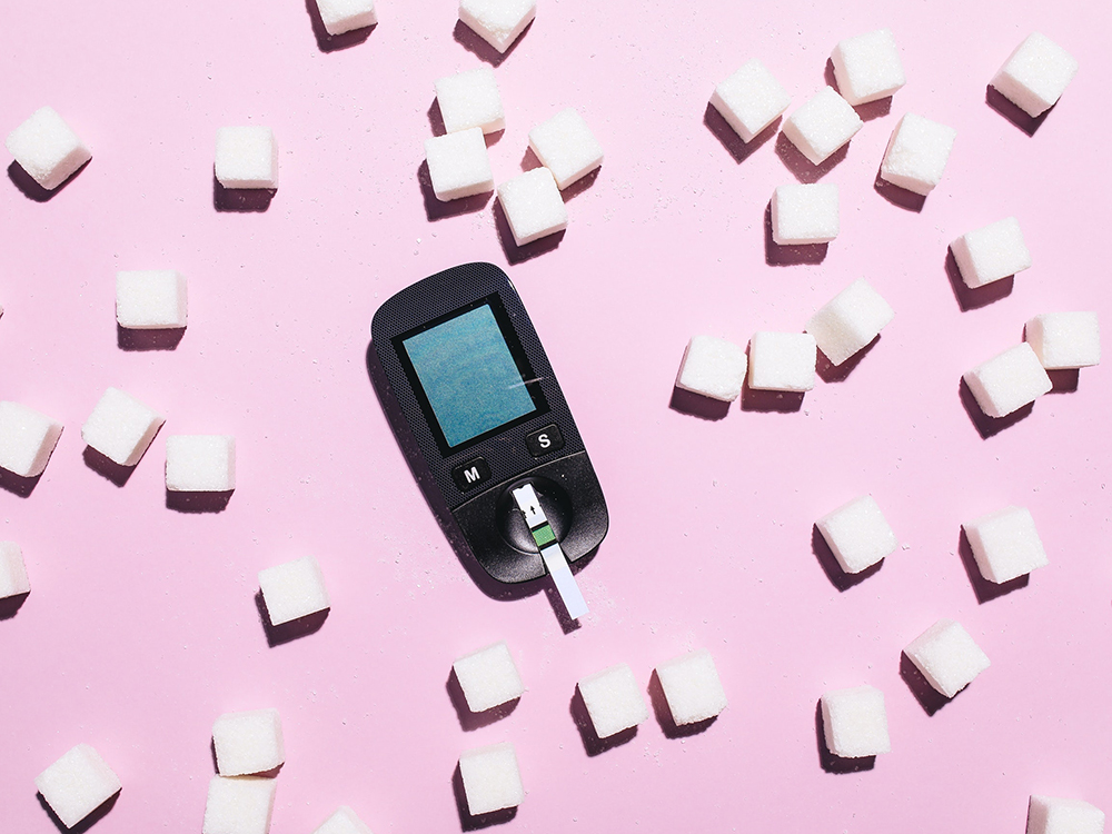 diabetes bloedsuikermeter afbeelding van bloedsuikermeter met roze achtergrond met suikerklontjes eromheen